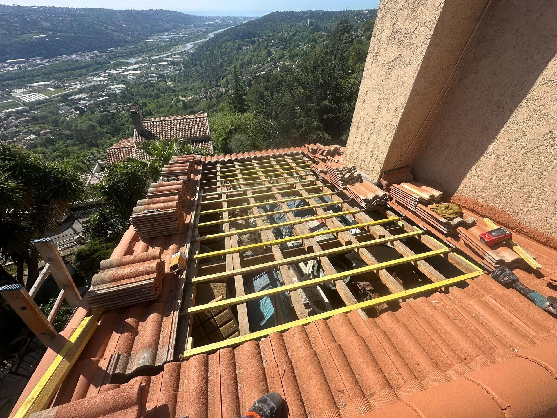 Toit aux poutres et tuiles apparentes, surplombant une vallée verdoyante baignée de soleil.