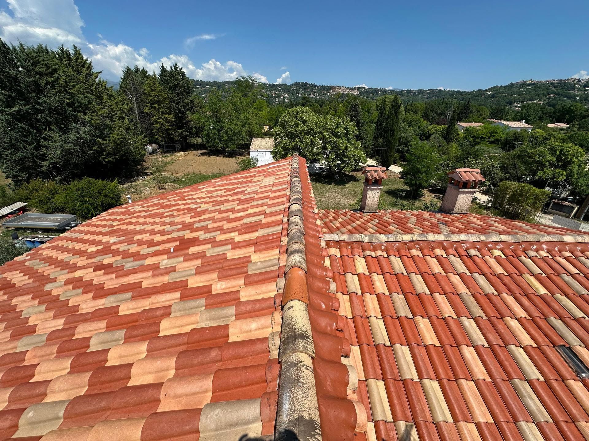 Toits de tuiles en terre cuite surplombant une colline verdoyante sous un ciel d'un bleu limpide