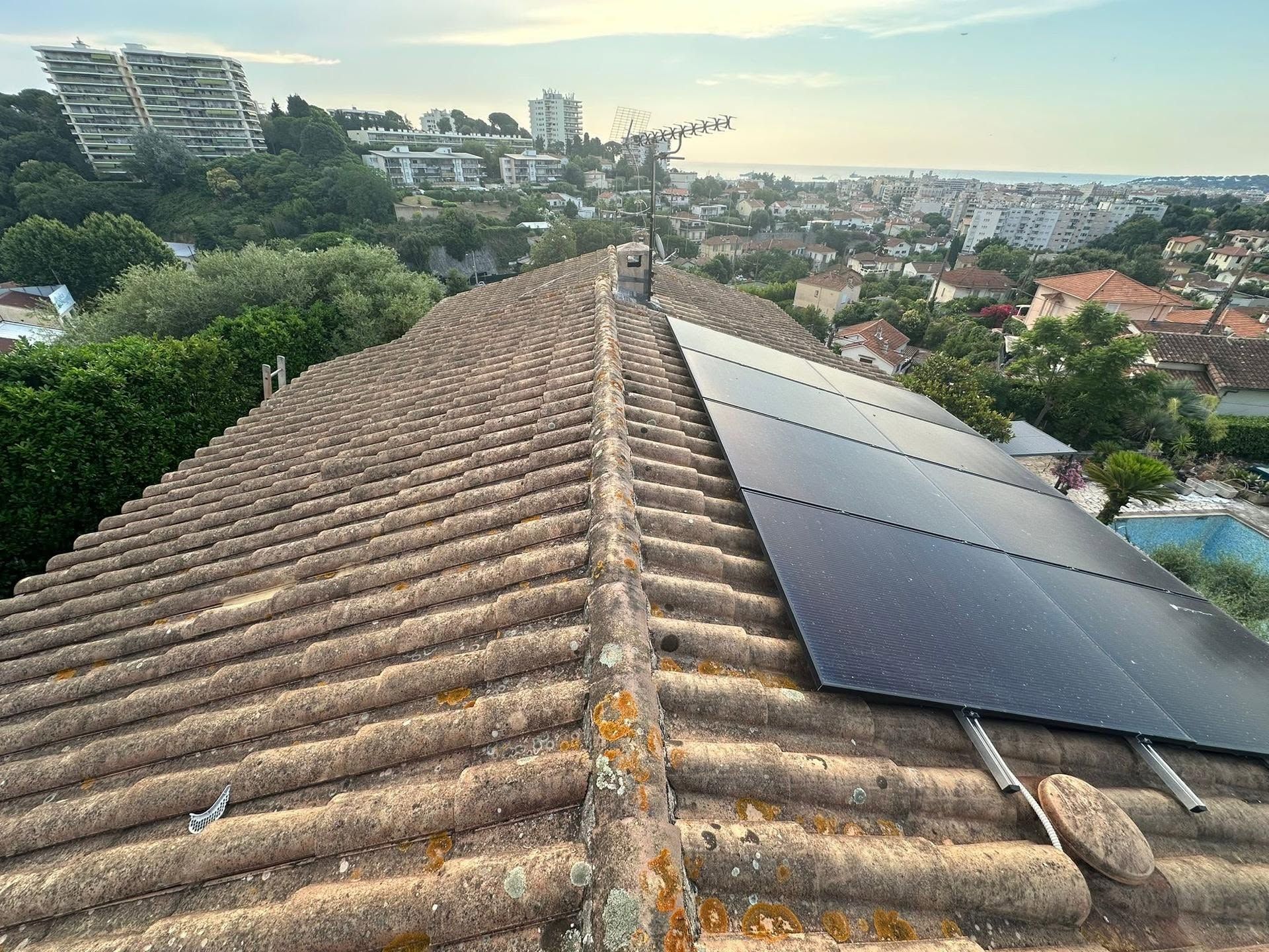 Toit-terrasse avec panneaux solaires donnant sur une ville et des collines verdoyantes au coucher du soleil