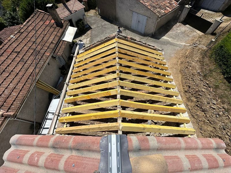 Toiture en construction avec charpente en bois jaune et toitures de tuiles environnantes, vue du dessus