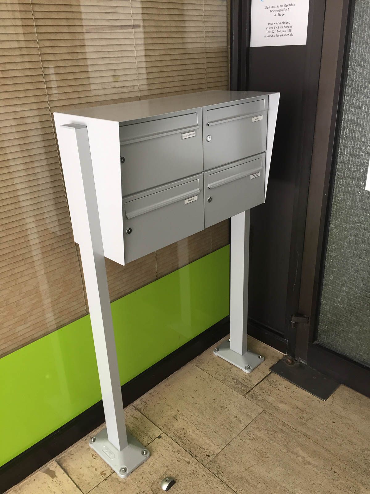 Vor einer grünen Wand steht ein weißer Briefkasten.