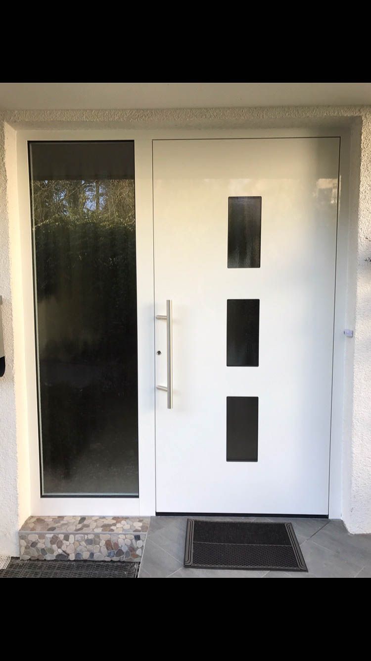 Eine weiße Tür mit drei Quadraten darauf und einer schwarzen Matte auf dem Boden.