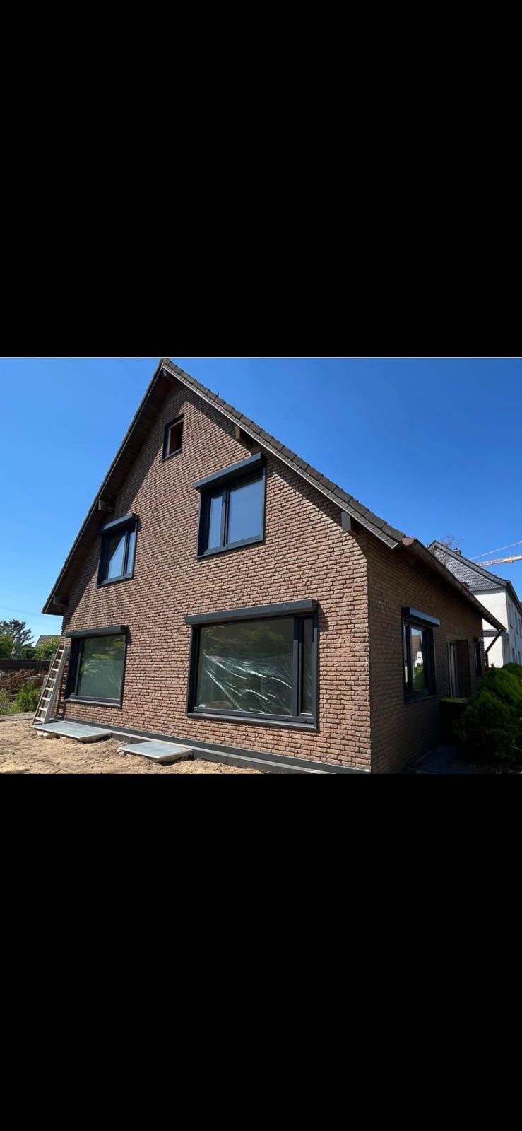 Ein Backsteinhaus mit schwarzen Fenstern und einem blauen Himmel im Hintergrund.
