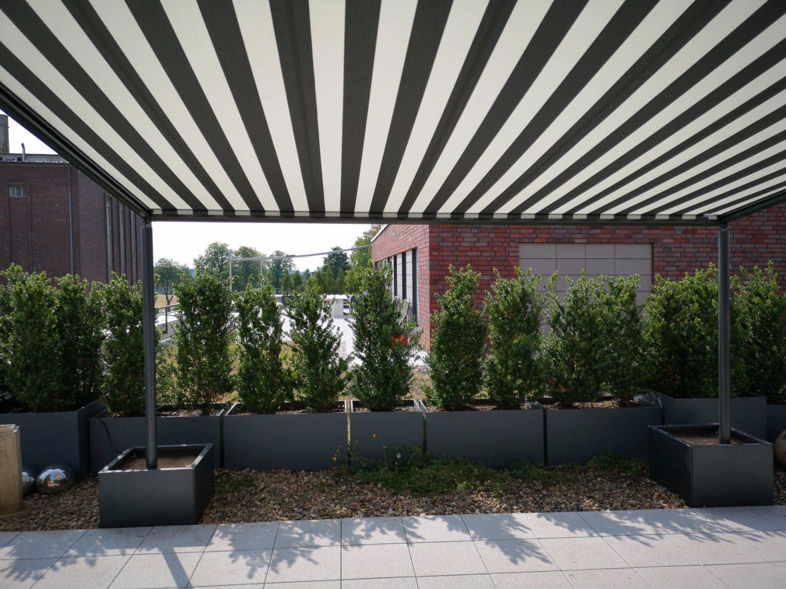 Eine schwarz-weiß gestreifte Markise über einer Terrasse mit Topfpflanzen