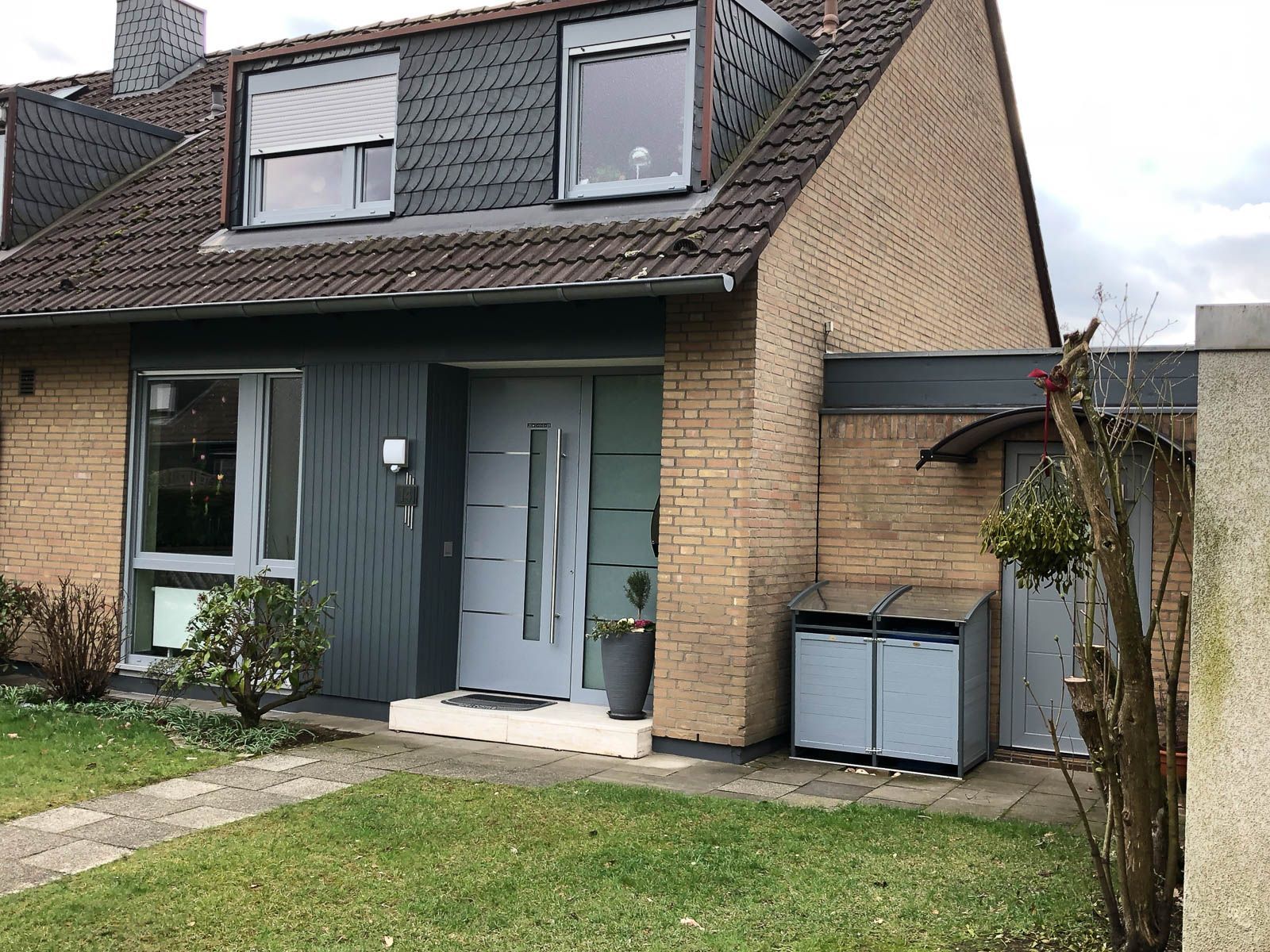 Ein Backsteinhaus mit einer grauen Tür und einer Mülltonne davor.
