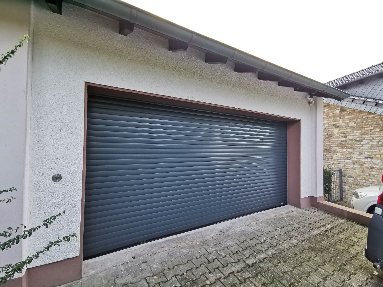 Vor einem Garagentor ist ein Auto geparkt.