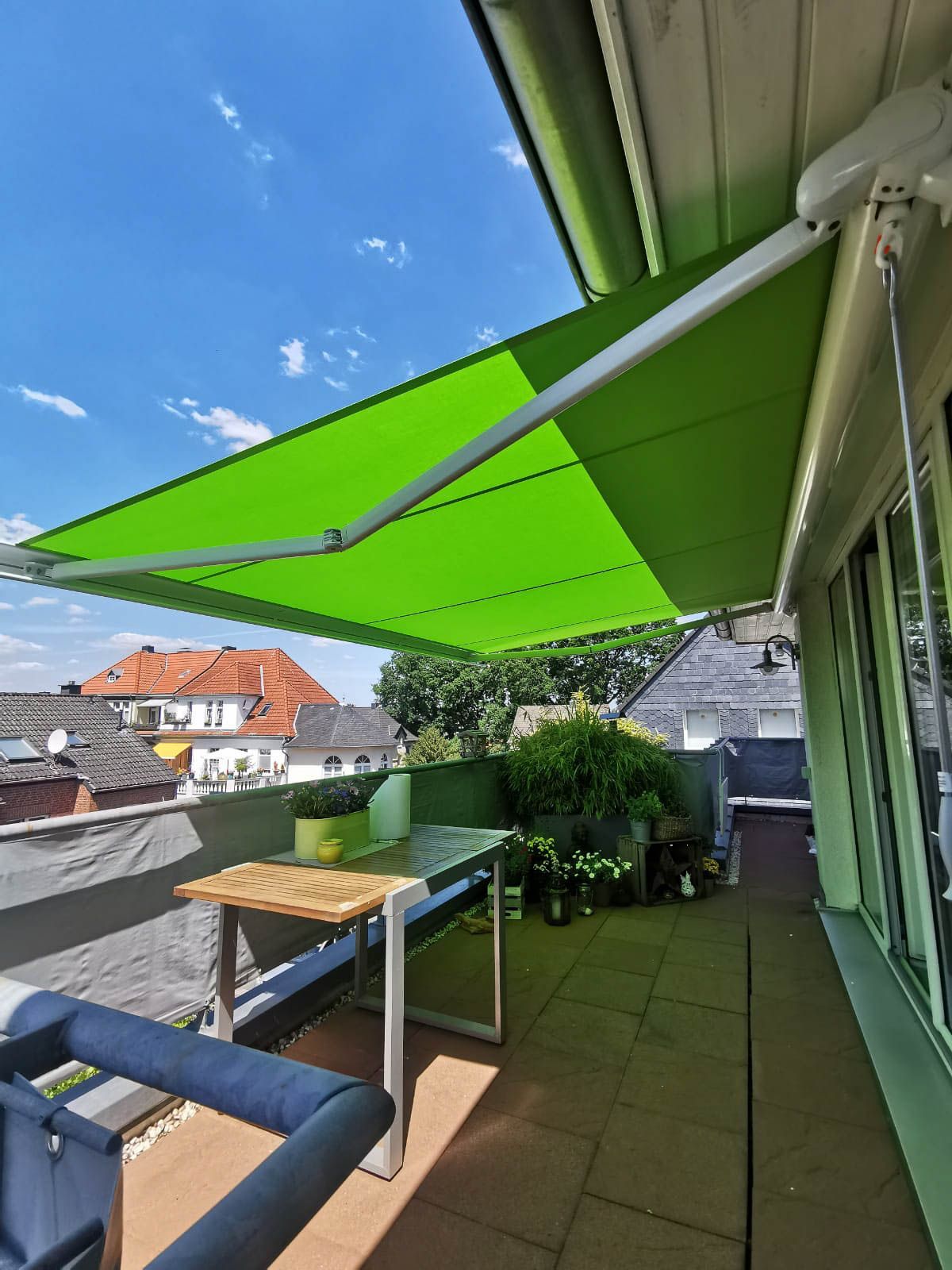 Eine grüne Markise überdacht einen Balkon mit Tisch und Stühlen.