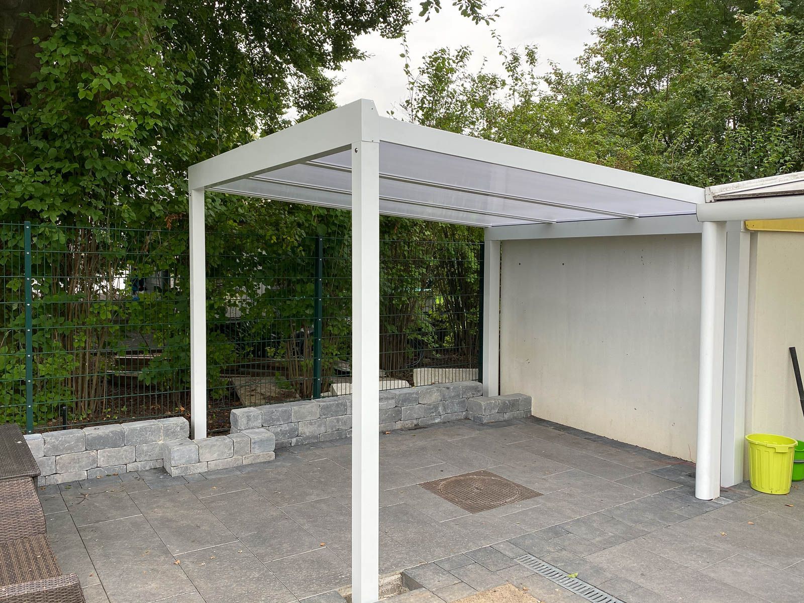 Auf einer Betonterrasse neben einem Haus steht eine weiße Pergola.