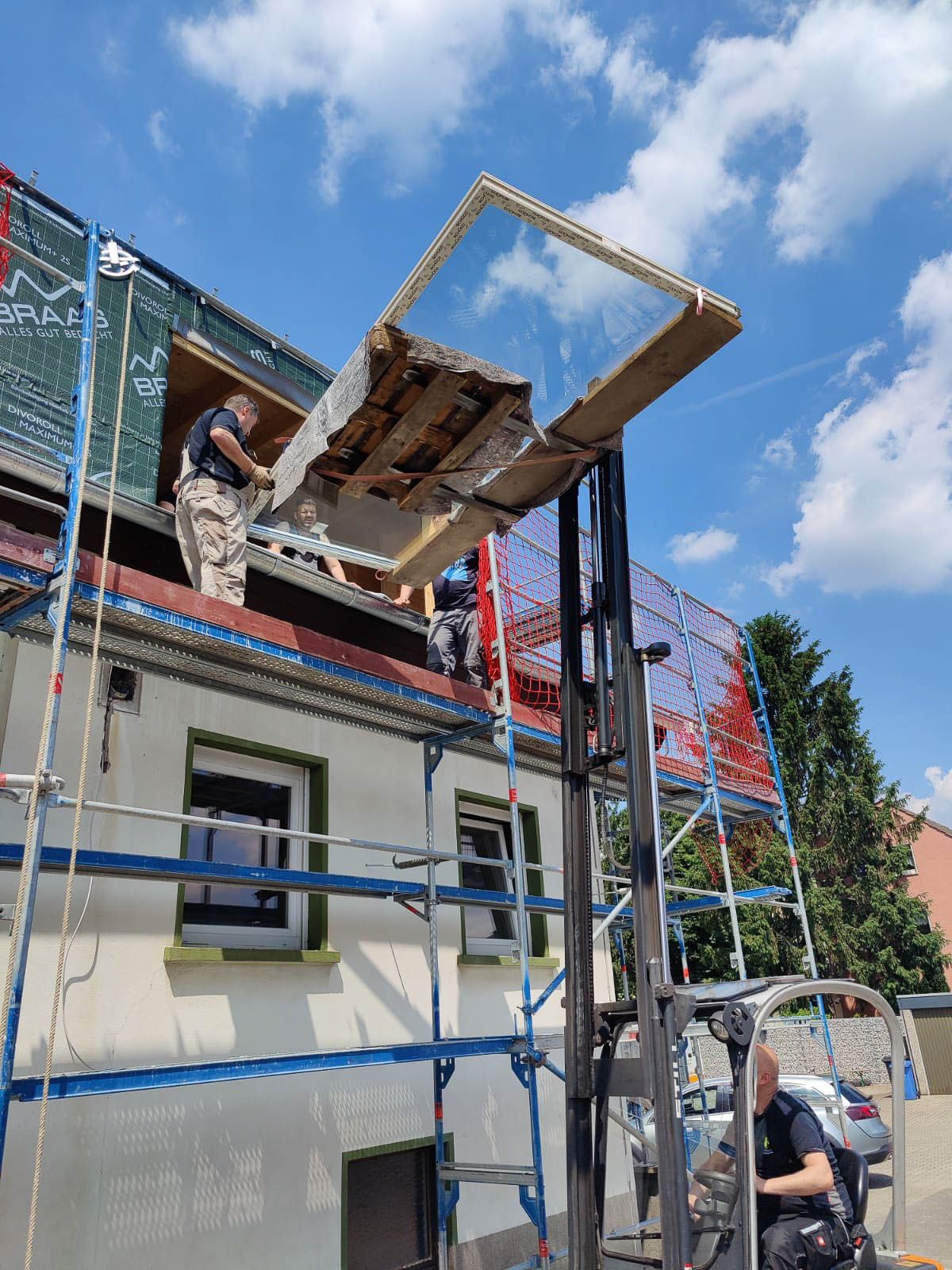 Ein Gabelstapler hebt ein Stück Holz auf ein Gebäude.
