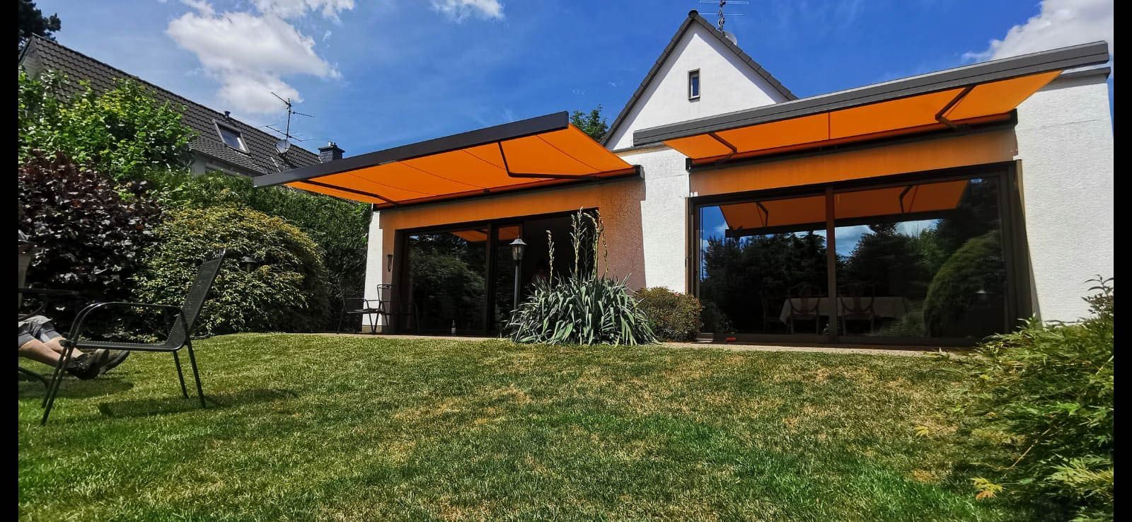 Ein Haus mit einer großen Wiese davor und einer orangefarbenen Markise.