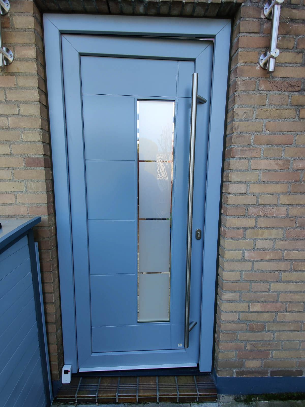 An einem Backsteingebäude befindet sich eine blaue Tür mit einem Edelstahlgriff.