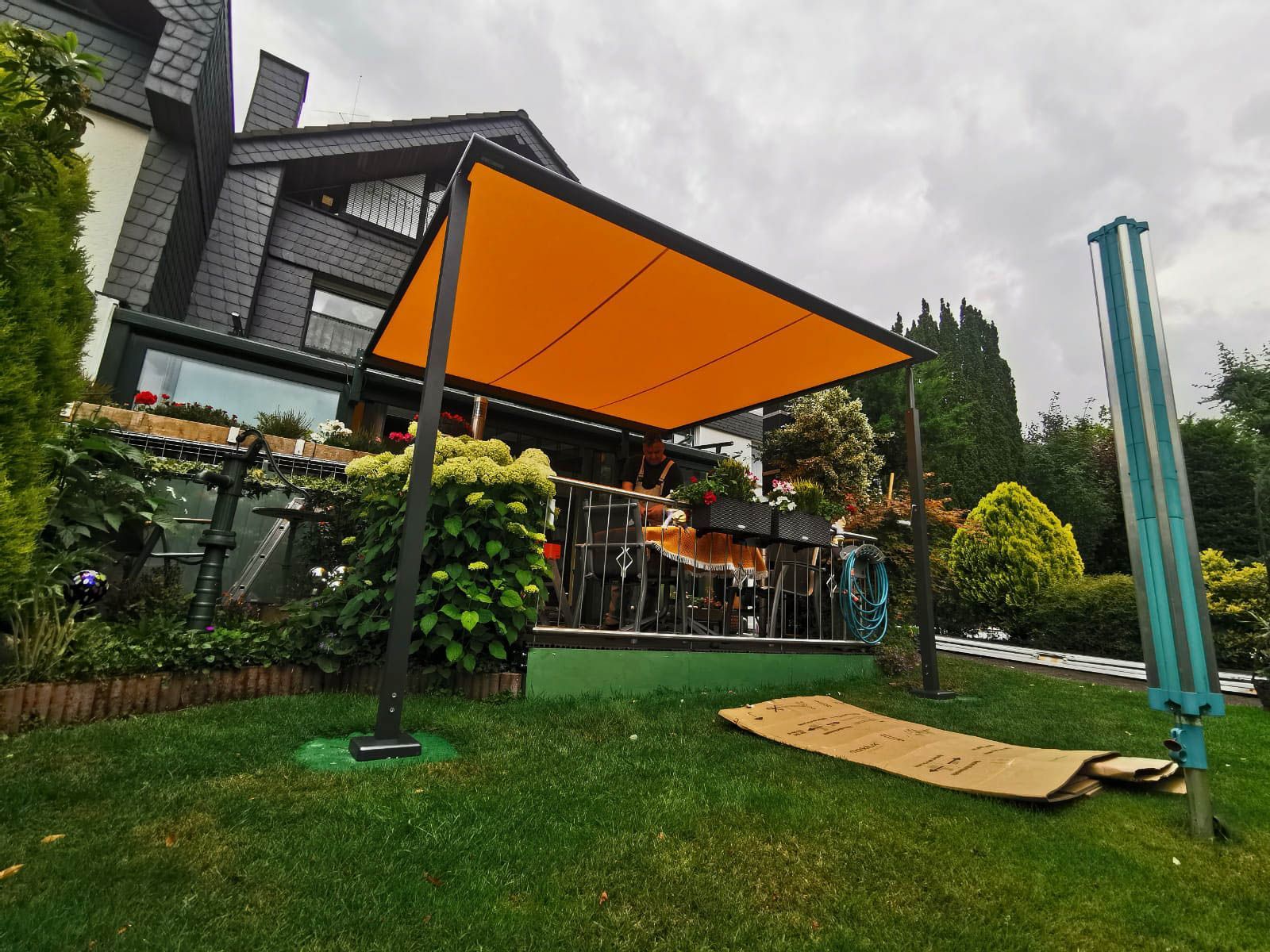 Auf einem üppigen grünen Rasen vor einem Haus steht eine große orangefarbene Markise.