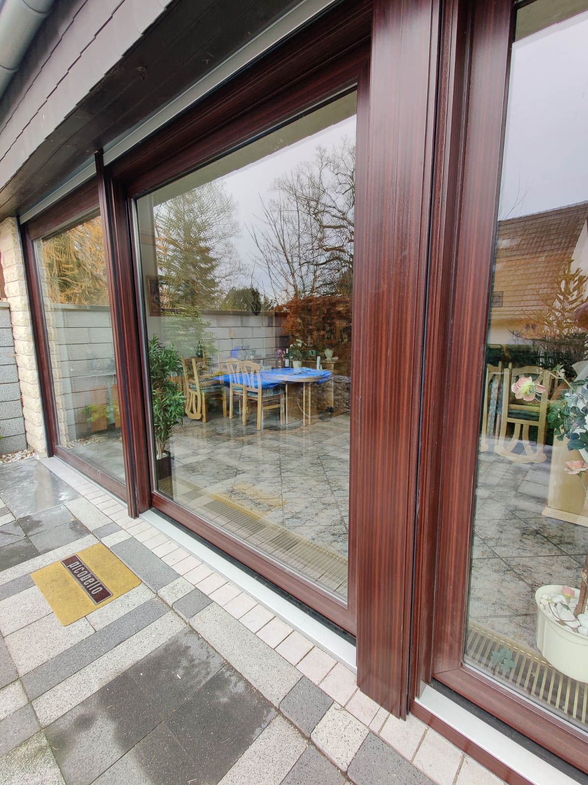 In den Fenstern eines Hauses spiegelt sich eine Terrasse mit Tisch und Stühlen.