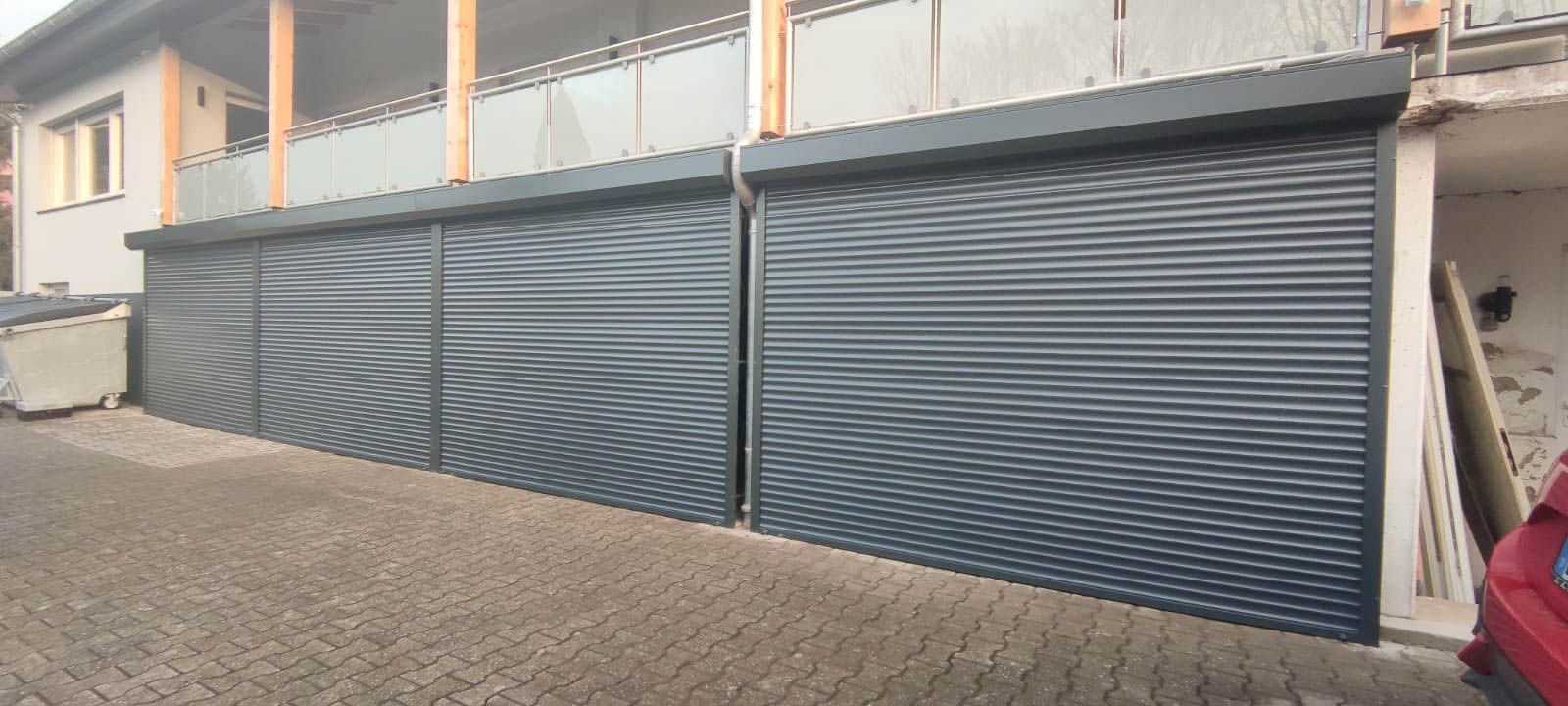 Ein rotes Auto parkt vor einem Gebäude mit Garagentor.