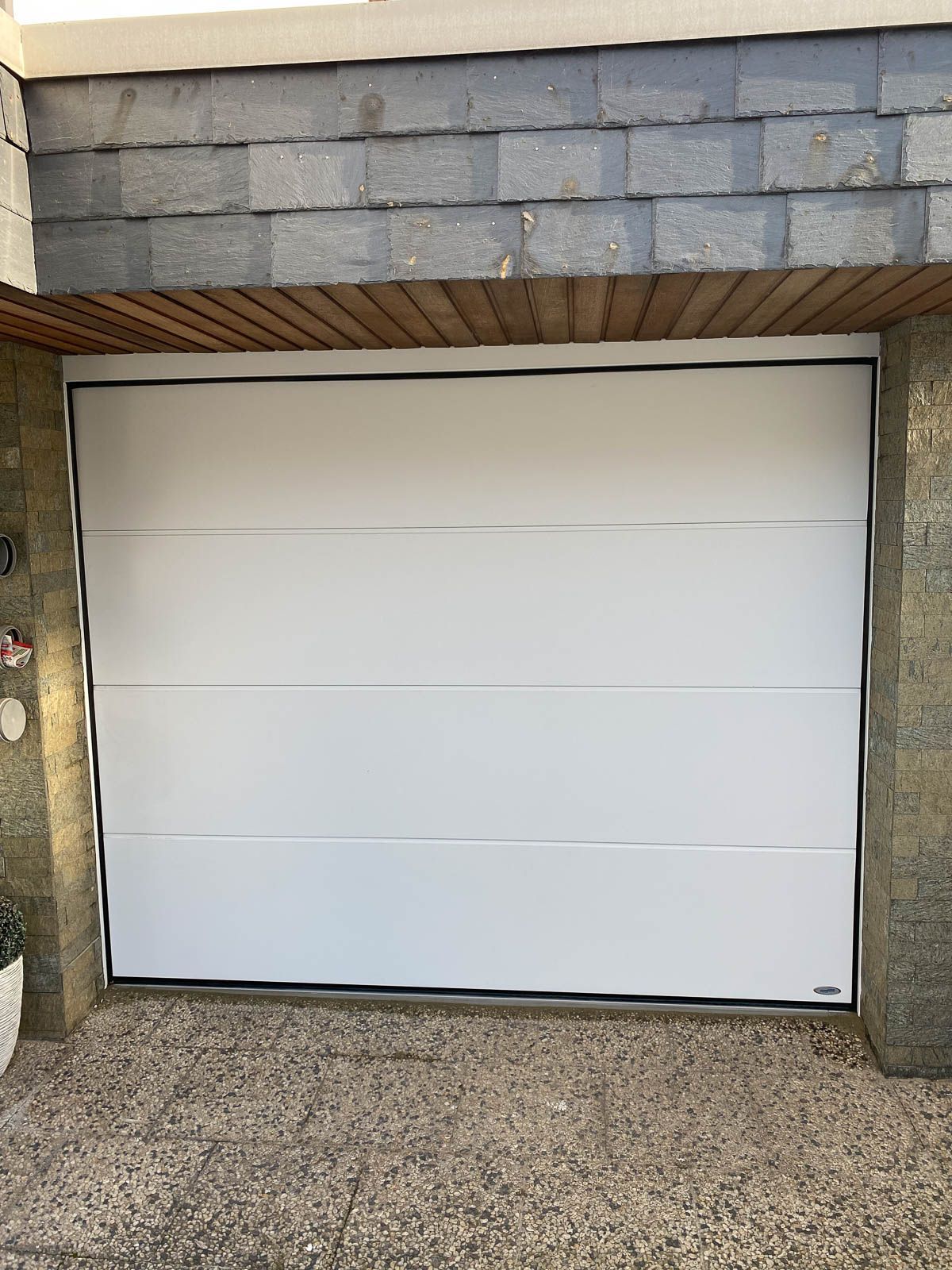 Vor einem Backsteingebäude steht ein weißes Garagentor.