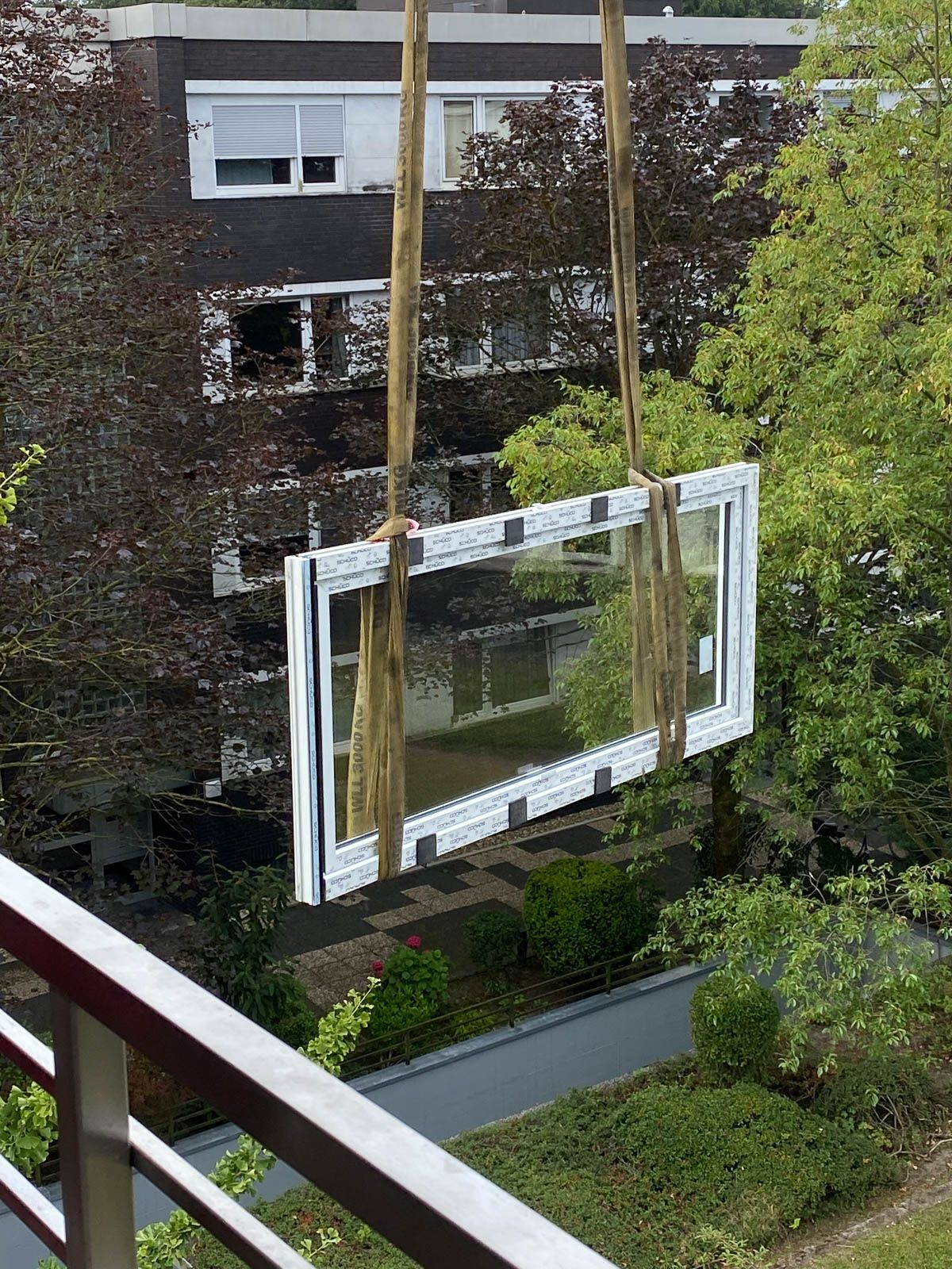 Vor einem Gebäude wird ein großes Fenster von einem Kran angehoben.