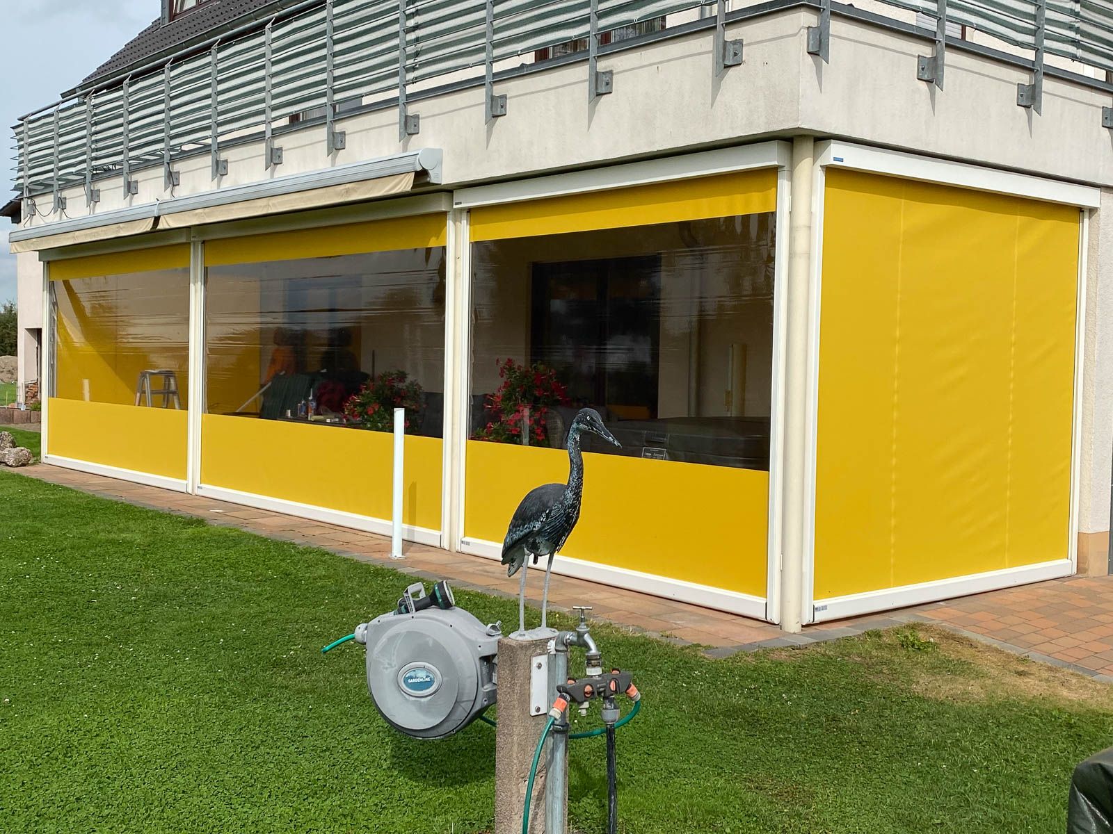 Ein Vogel steht vor einem Haus mit gelben Vorhängen.