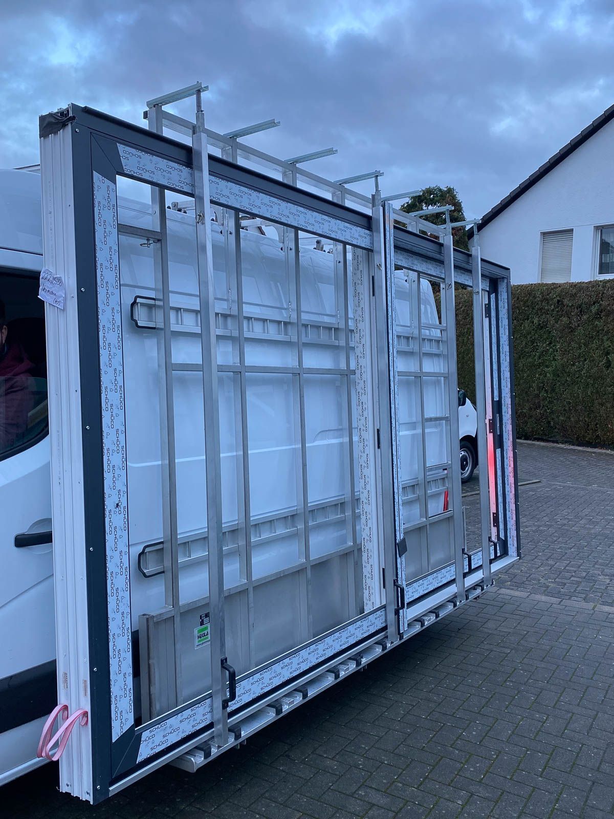 Auf einem Parkplatz steht ein weißer Lieferwagen mit einem großen Fenster an der Rückseite.