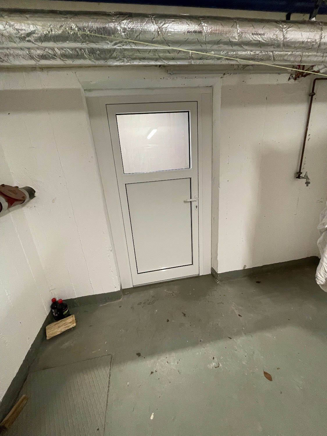 In einem Raum befindet sich eine weiße Tür mit einem Glasfenster.