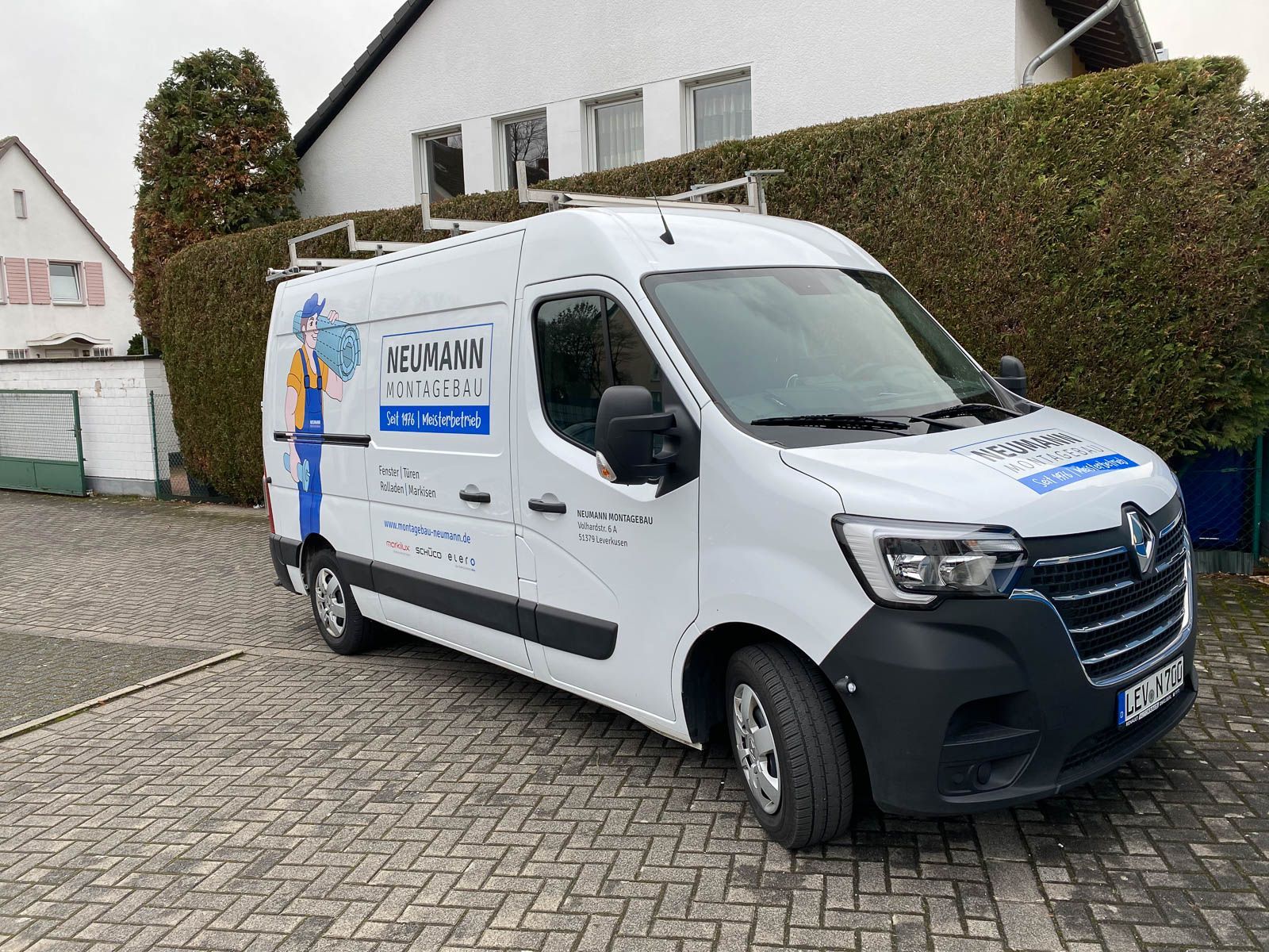 Ein weißer Lieferwagen steht auf einer gepflasterten Auffahrt vor einem Haus.