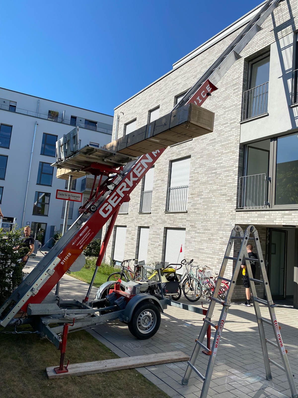 Vor einem Gebäude steht neben einem Kran eine Leiter.