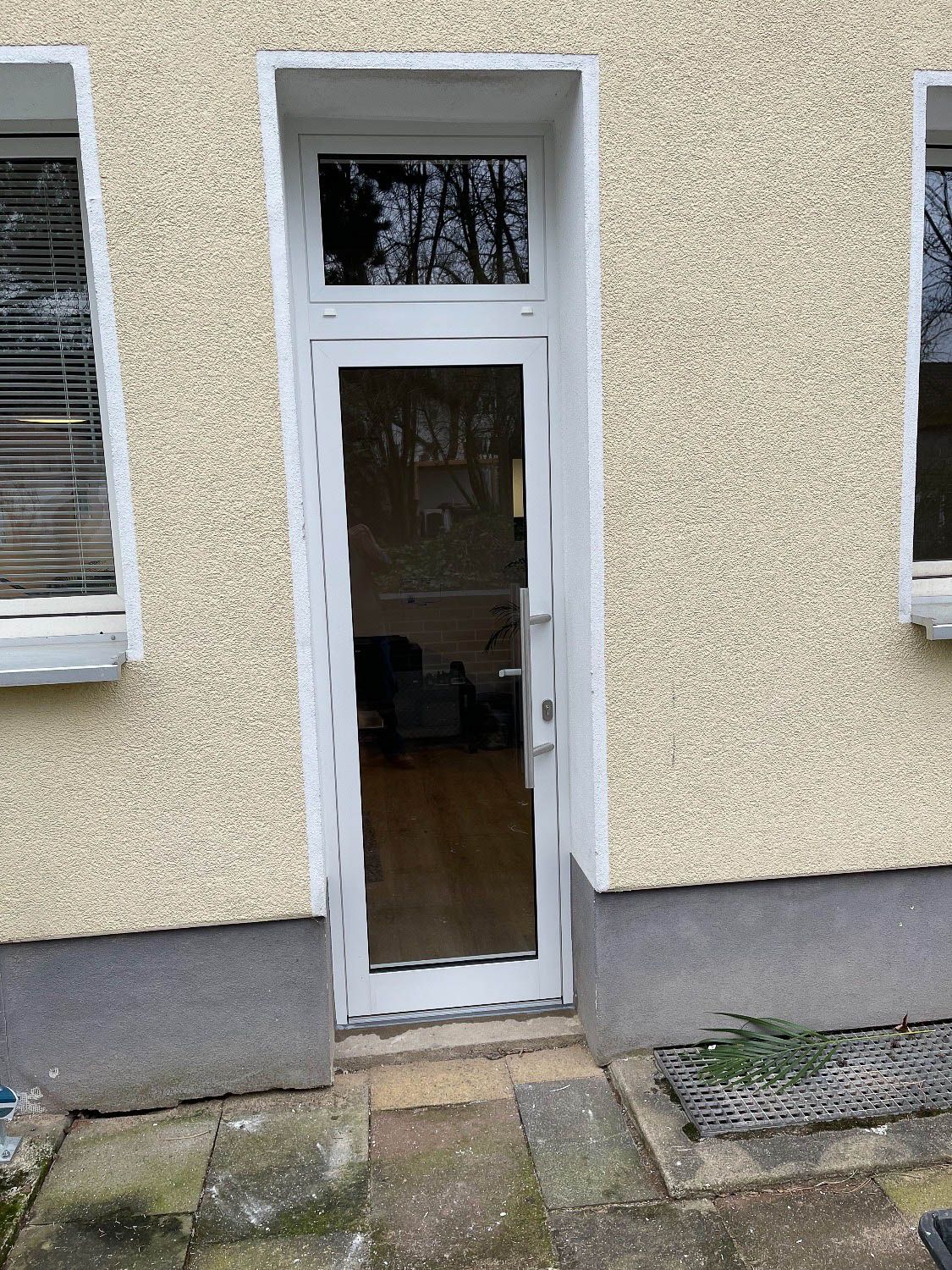 An der Seite eines Gebäudes befindet sich eine weiße Tür mit Glasscheibe.