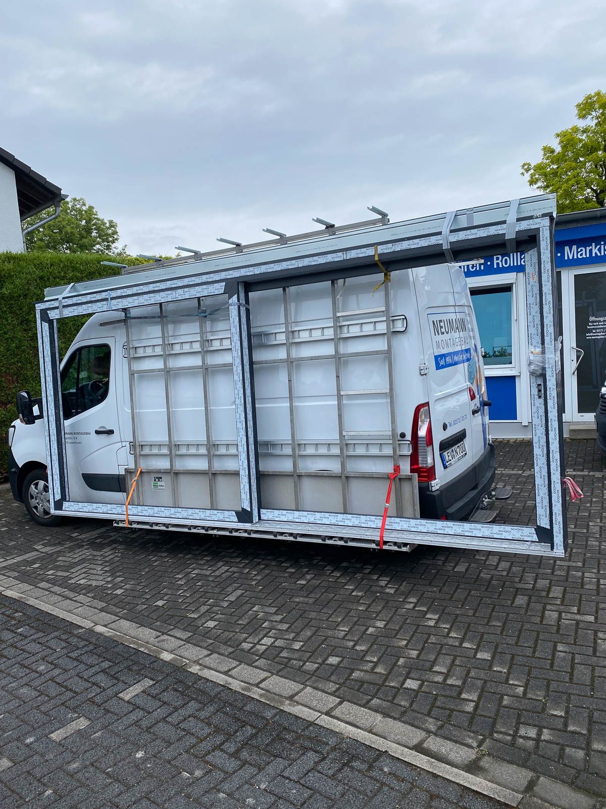 Ein weißer Lieferwagen parkt auf einem gepflasterten Gehweg neben einem Gebäude.