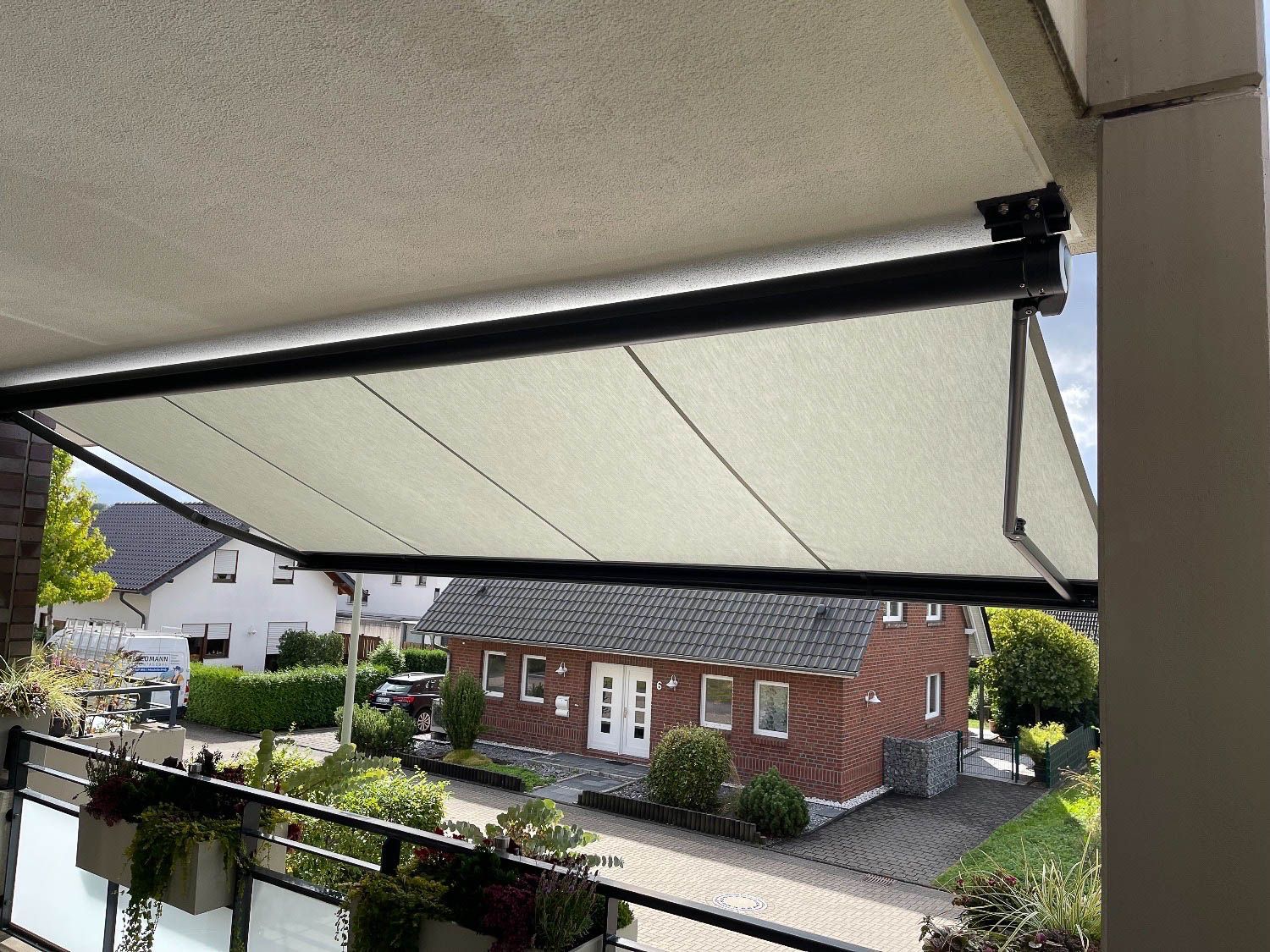 Ein Balkon mit einer weißen Markise darüber und einem Backsteinhaus im Hintergrund.
