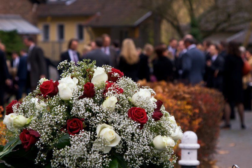 Un ramo de rosas rojas y blancas con flores de aliento del bebé frente a una multitud de personas.