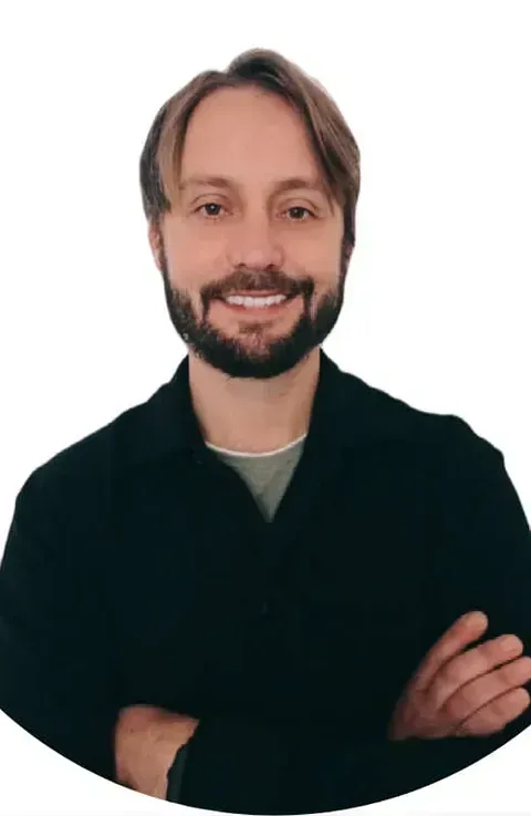 Un hombre con barba sonríe con los brazos cruzados.