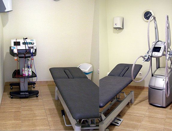 Sala médica con mesa de exploración, equipamiento y reloj de pared.