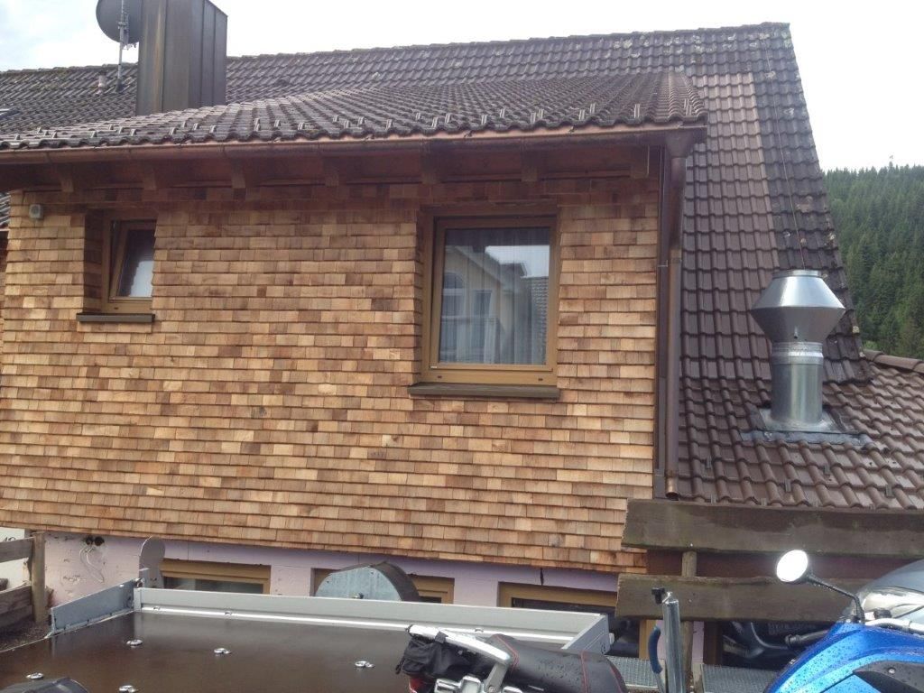 Nahaufnahme einer Holzfassade mit Fenster und metallischem Kaminrohr unter dem Dach