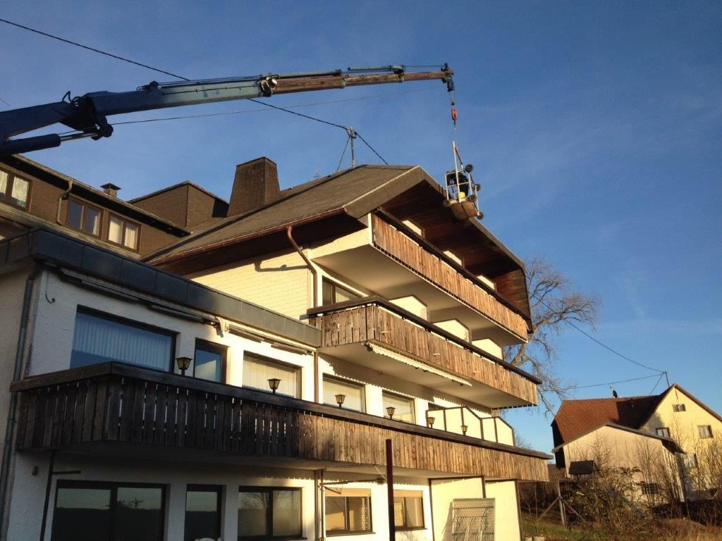 Kranarbeiten am Dach eines mehrstöckigen Wohnhauses mit Holzbal konen