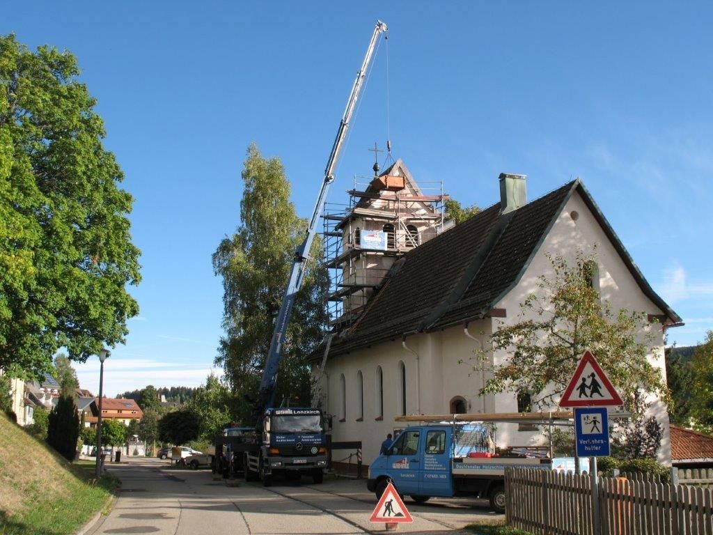 Ein Haus mit hohem Satteldach, Dachreiter und Gerüst im Hintergrund unter blauem Himmel
