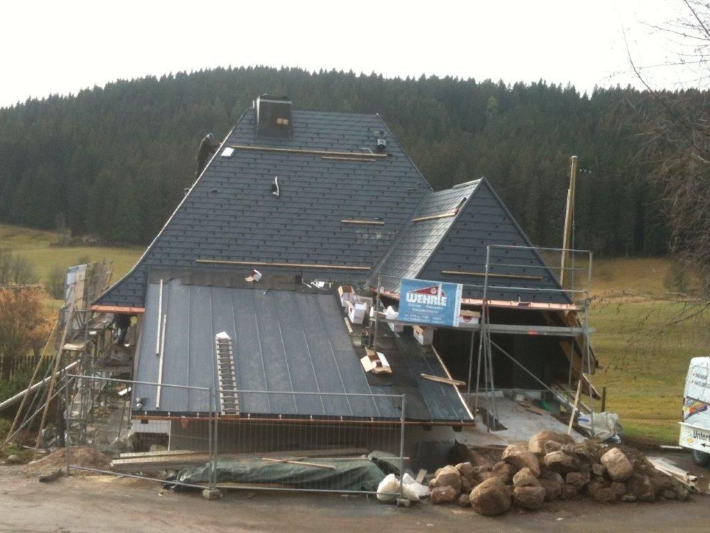 Ein Holzrahmenbau-Haus während der Dachdeckungsarbeiten, mit Gerüst und Schieferplatten