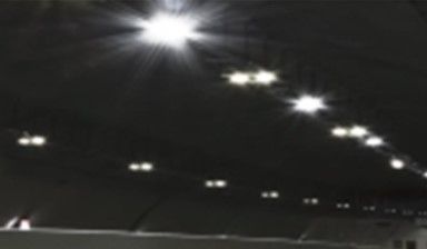 Un techo oscuro con una hilera diagonal de luces brillantes y resplandecientes de estadio que iluminan hacia abajo.
