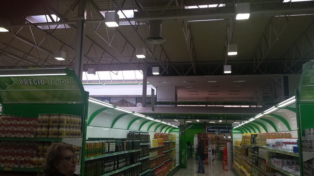 Vista en perspectiva de un pasillo de un supermercado con estanterías decoradas en verde e iluminación.