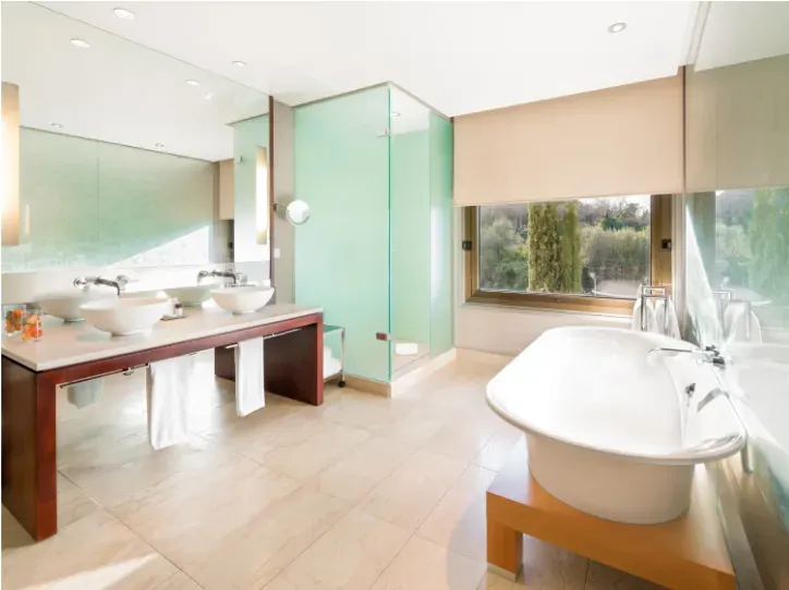 Un baño moderno con lavabo doble, ducha con mampara de cristal y bañera blanca junto a una gran ventana.