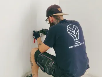Un electricista, con una camiseta negra de marca, se arrodilla para instalar