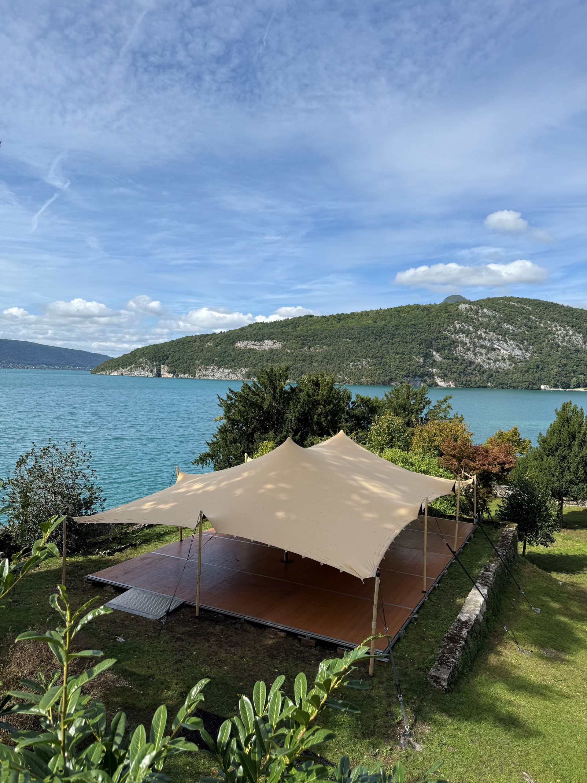 Une tente beige sur une plateforme en bois surplombant un lac et des montagnes sous un ciel bleu.