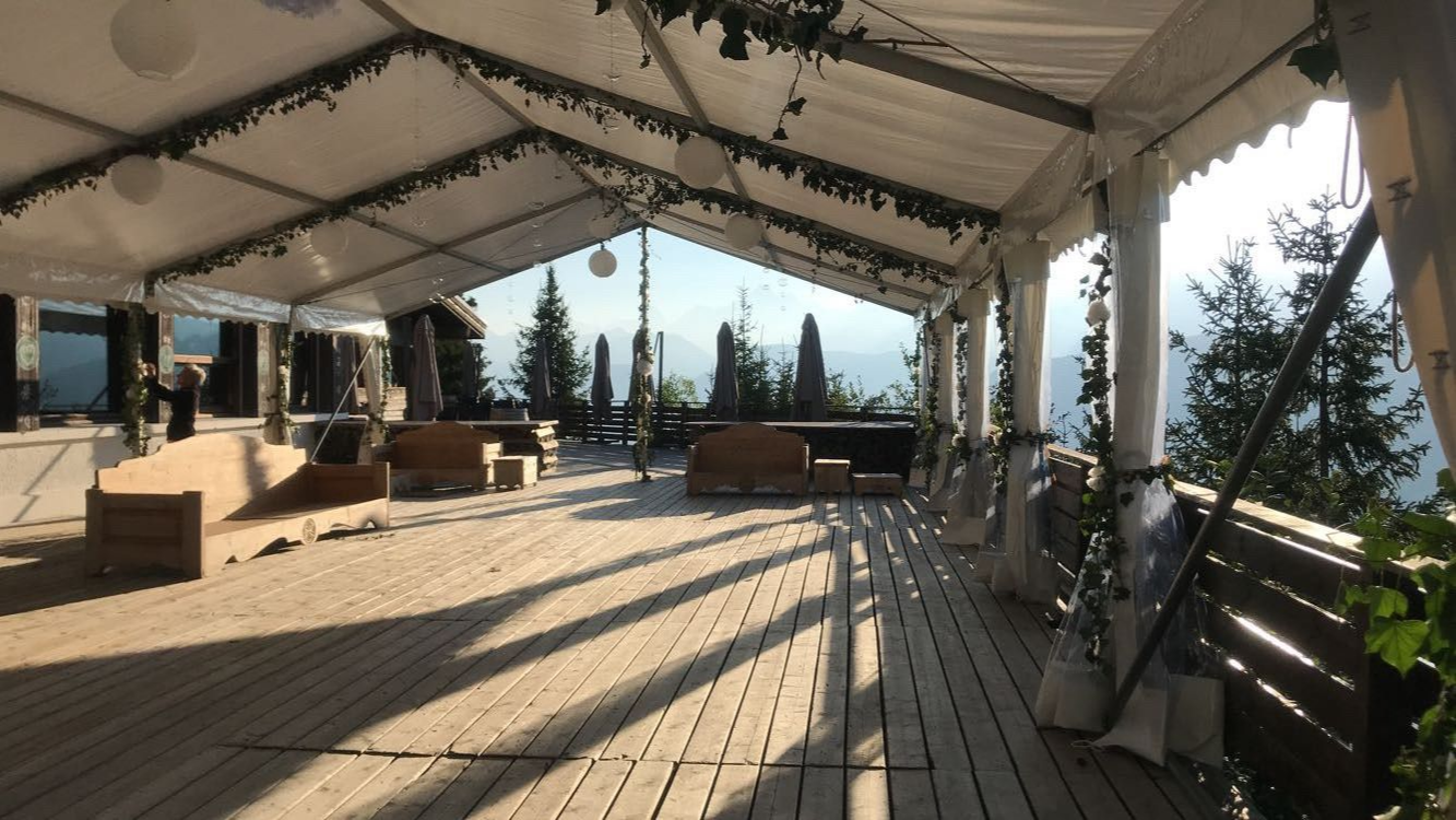 Terrasse en bois sous la tente avec vue sur la montagne ; espaces de détente et feuillage décoratif.