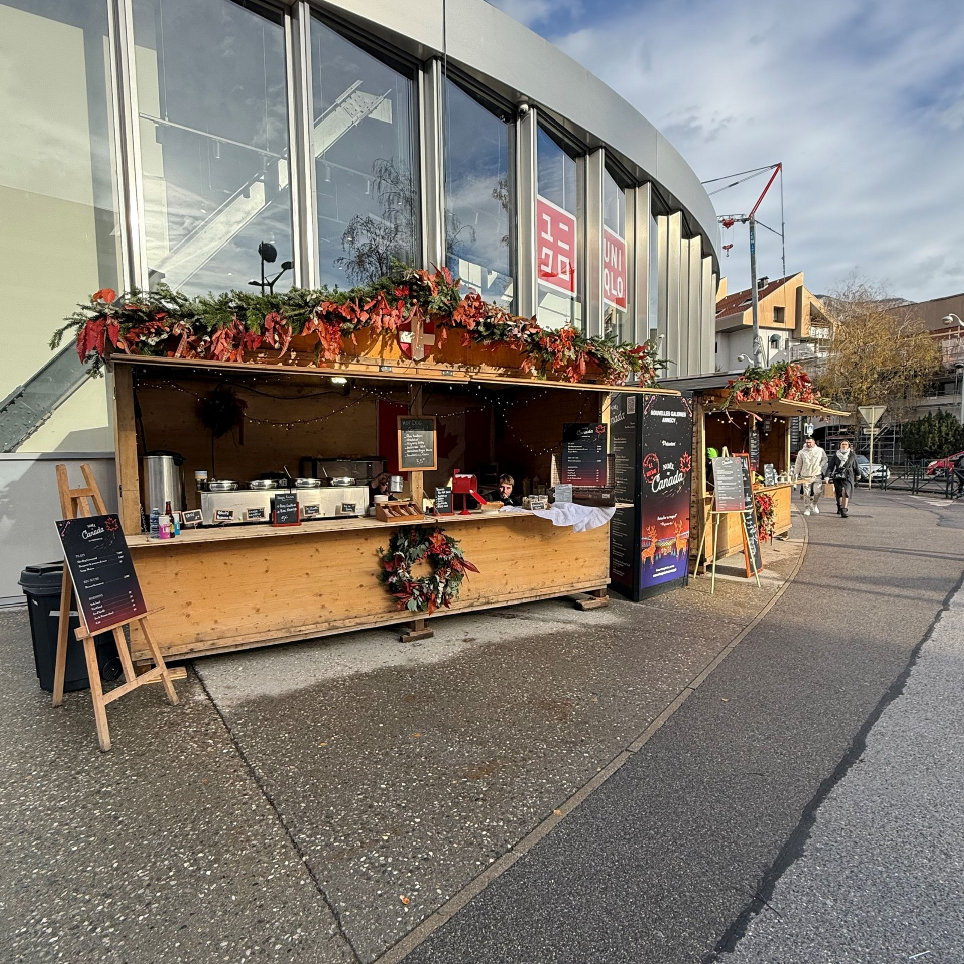 Des stands de marché de Noël décorés de guirlandes devant un bâtiment moderne.