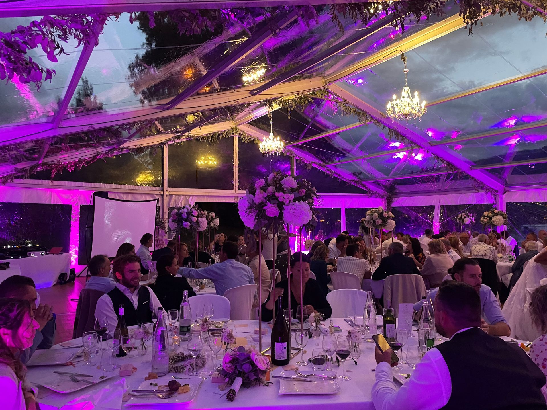 Une grande tente transparente est installée à flanc de colline, devant un château.