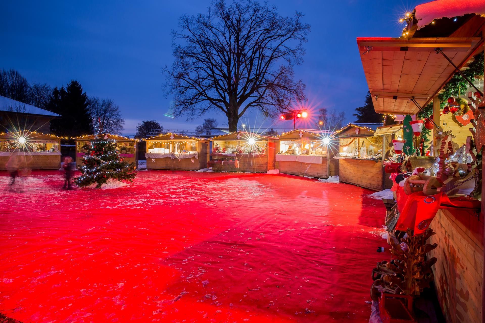 Des étals de marché en bois vides sont alignés sur une aire pavée, avec une table de pique-nique au premier plan.