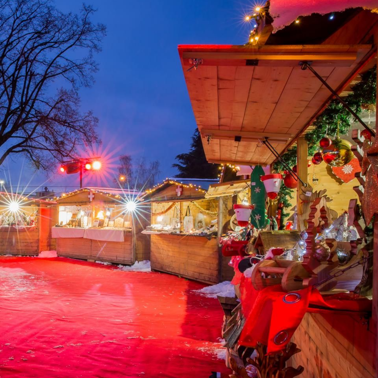 Des stands de marché de Noël illuminés, décorés et avec un sol rouge au crépuscule.