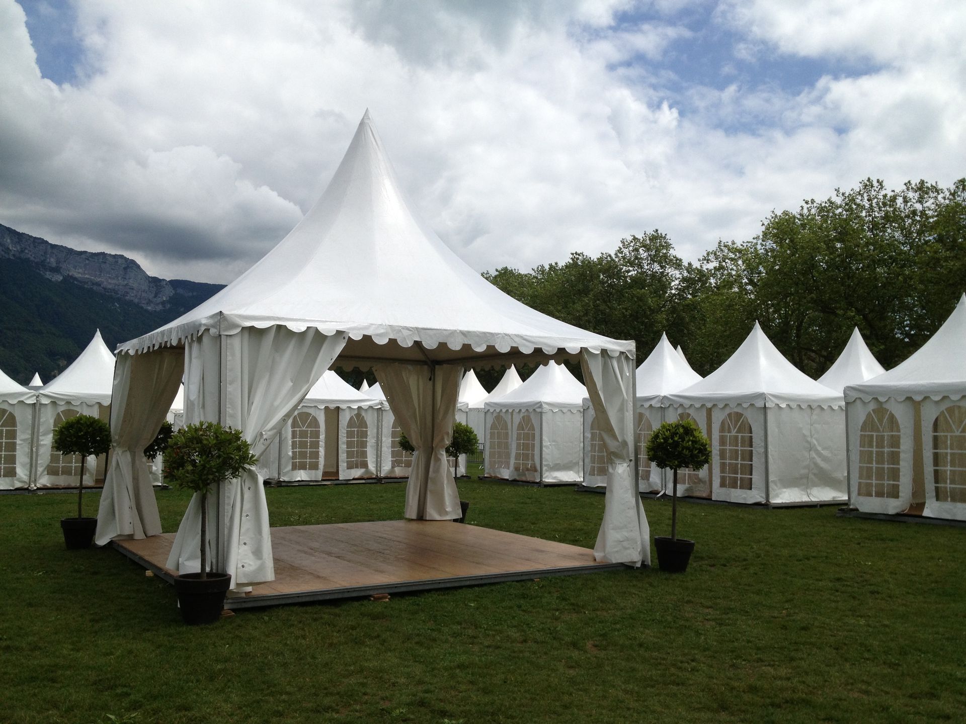 Des tentes blanches dressées sur l'herbe verte pour un événement ; des montagnes en arrière-plan.