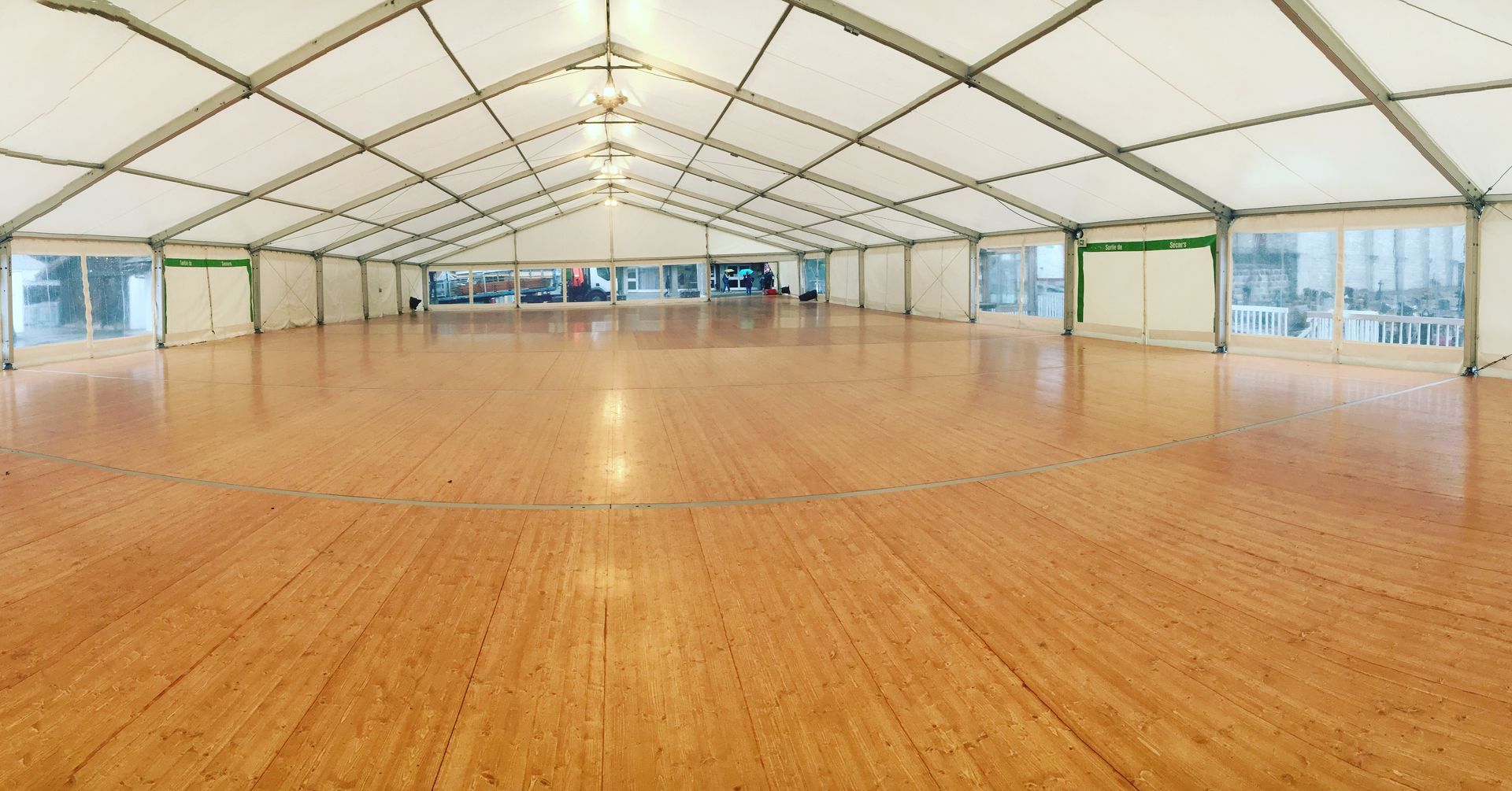 Grande tente vide avec un sol en bois clair et des murs/plafond blancs. Le sol reflète la lumière.