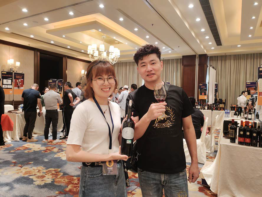 Dos personas sonriendo y sosteniendo copas de vino en un banquete de hotel.
