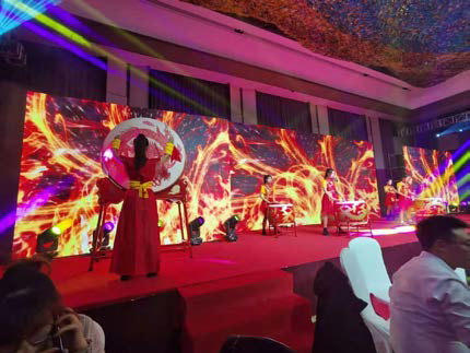 Actuación escénica con un artista vestido de rojo bajo brillantes proyecciones visuales abstractas.