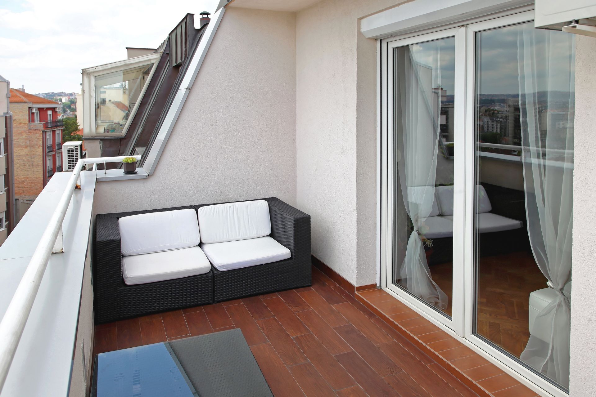 Balcon avec canapé en osier, terrasse en bois et baie vitrée.
